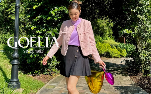 a lady in a purple top, a pink tweed jacket, a grey pleated skirt and a pair of sneakers