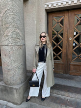 A lady wears a trench coat and white pants.