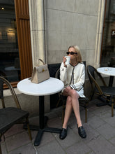 A woman in a white cardigan sitting in front of a coffee shop.