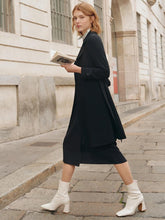 A lady wears a black trench coat.