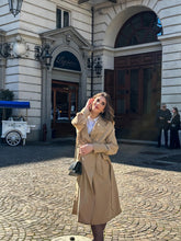 A lady wears a camel trench coat.