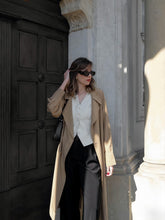 A lady wears a vest and a trench coat.