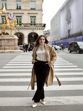 A lady wears flared pants and a trench coat.