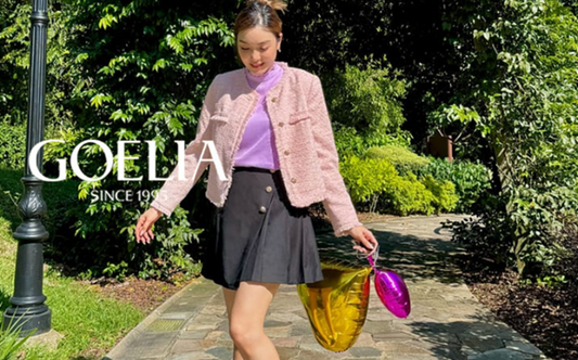 a lady in a purple top, a pink tweed jacket and a grey pleated skirt